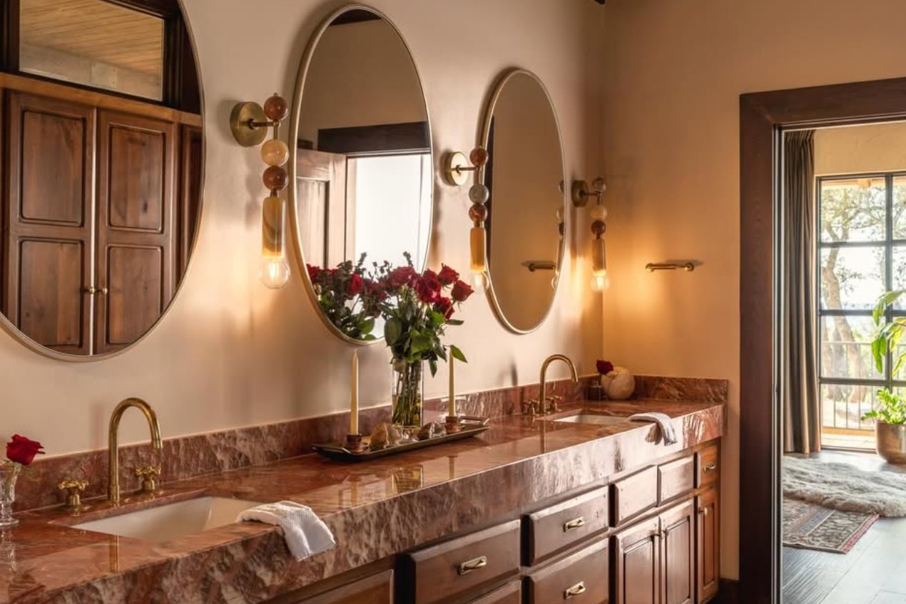 Bathroom with pink marble counters, oval mirrors and brass fixtures