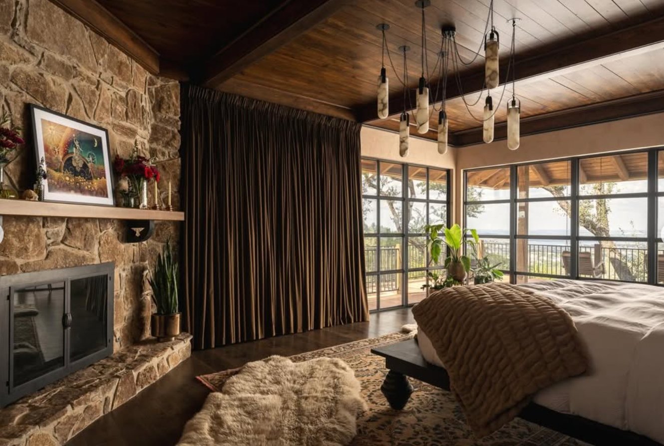 Bedroom with stone fireplace and large windows looking over the hills