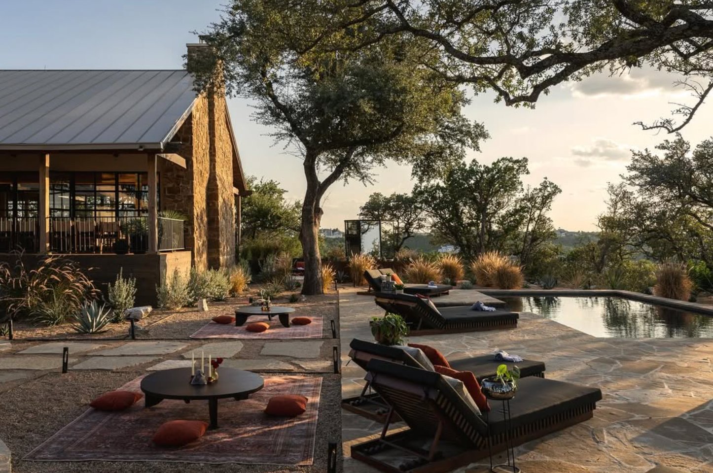 Outdoor pool at sunset with stone house and oak trees